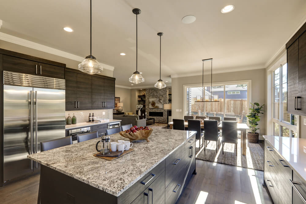Modern gray kitchen features dark gray cabinetry paired with white quartz countertops and a glossy gray linear tile backsplash. Bar style kitchen island with granite counter. Northwest, USA